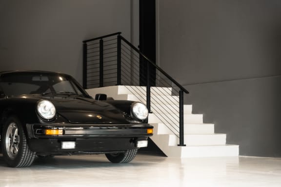 White stair in a gray showroom garage with black horizontal rod railing behind a classic black sports car.