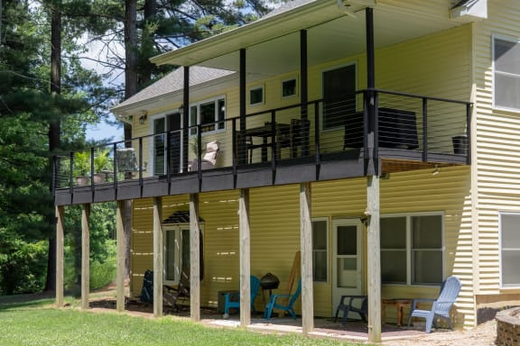 Black side-mounted cable railing on an elevated deck of a yellow home among pines.