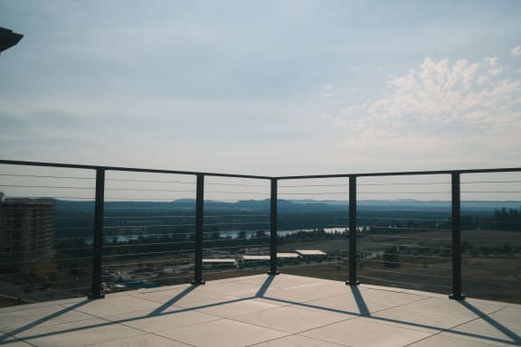 Black cable railing wraps a paved rooftop terrace overlooking a river valley.
