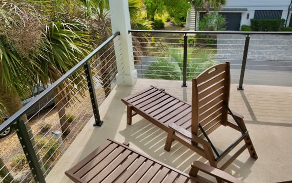 Black cable railing surrounds a balcony with wooden loungers overlooking palms.