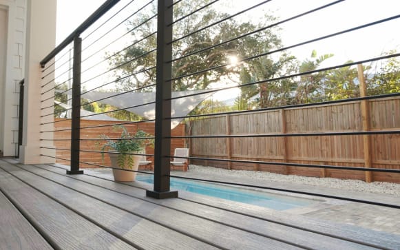 Low-angle view of black rod railing along a gray composite deck beside a narrow plunge pool.