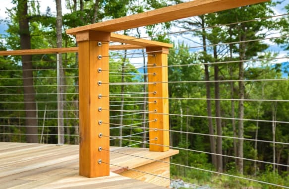 Cedar posts and cap rail with stainless cable infill around a wood deck in the forest.