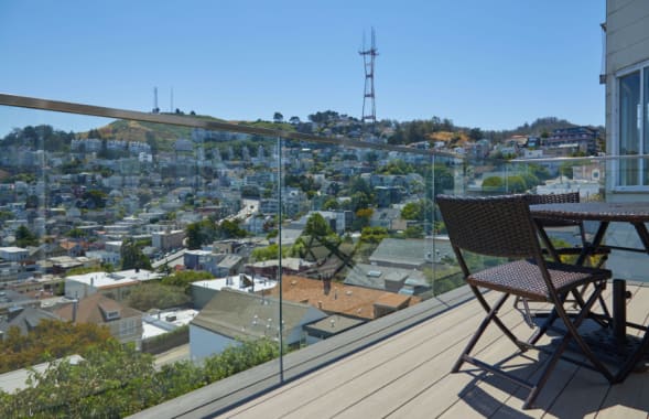 Frameless glass railing wraps a composite deck with bistro chairs overlooking hillside city homes and a radio tower.