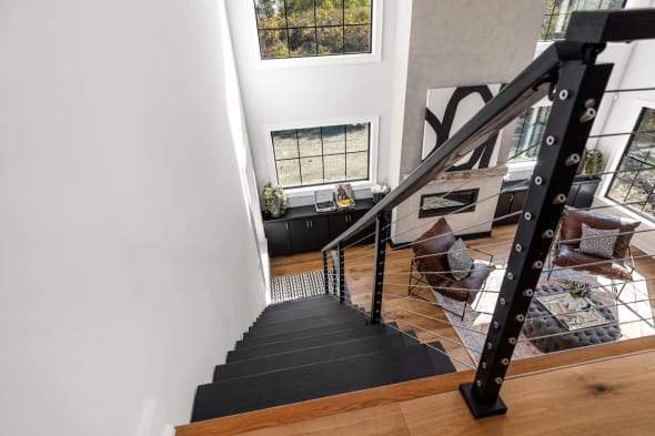 Black cable railing follows dark treads down into a bright living room with tall windows.
