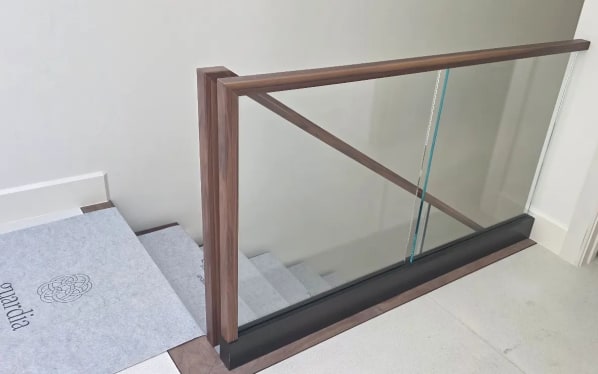 Frameless base rail glass with a walnut cap and squared walnut newel at the head of a stair