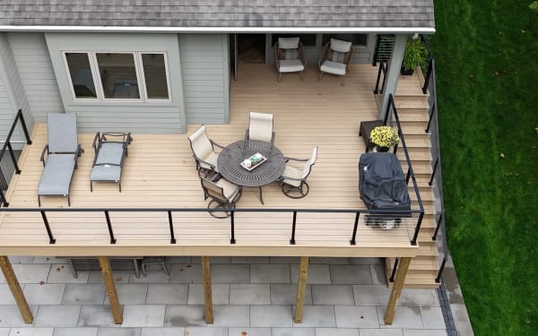 Overhead view of a tan composite deck with black cable railing, patio furniture and side stair above a stone patio.