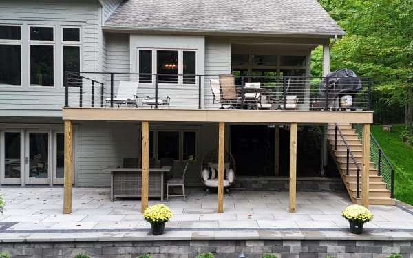 Elevated composite deck and stair with black cable railing above a stone patio.