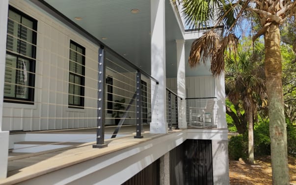 Cable railing runs between white structural porch posts on a coastal home among palms.