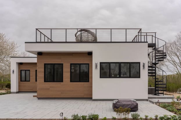 Black steel spiral stair climbs to a rooftop deck with cable railing on a modern white home.