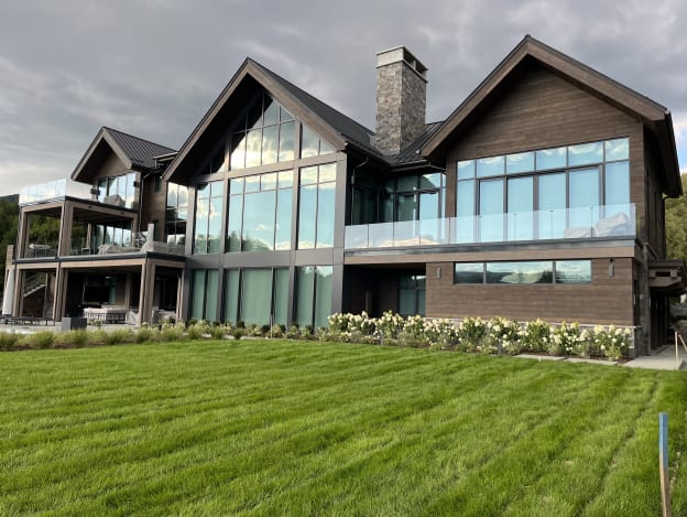 Timber and glass mountain home with frameless glass balcony railings above a green lawn