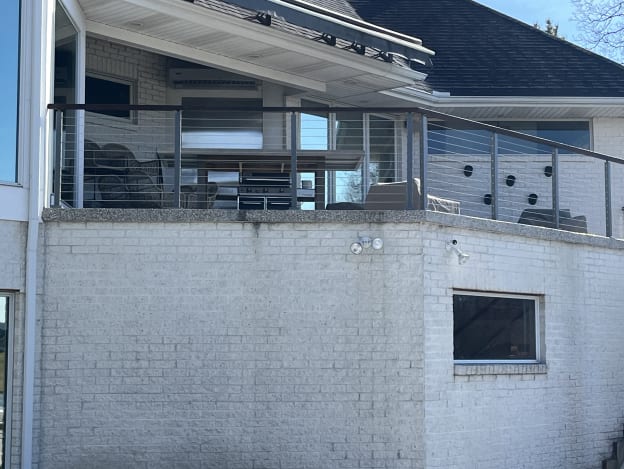 Gray-post cable railing with a dark top rail along a covered terrace on a white brick home