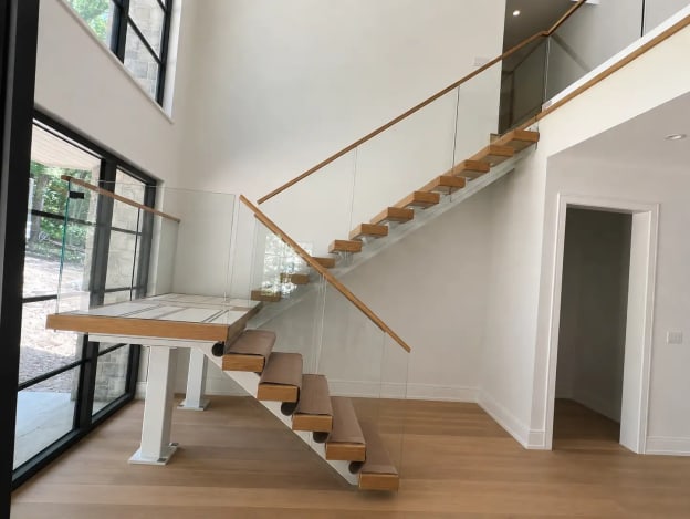 Oak floating treads with a landing on white posts rise to a loft behind frameless glass with oak handrail.