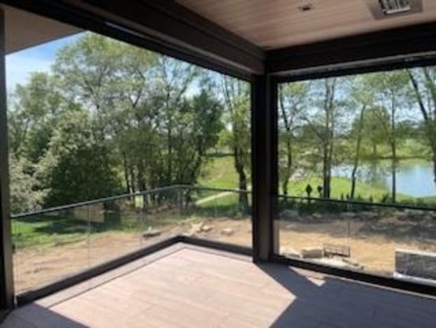 Frameless glass in a black base channel with black cap wraps the corner of a covered porch overlooking trees and a pond.