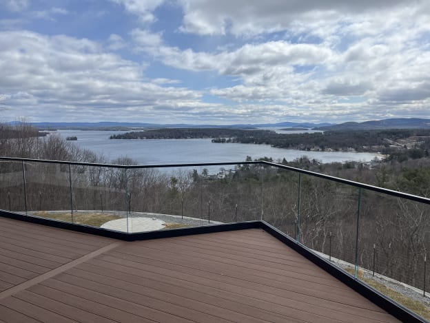 Black base-rail glass with black top cap angles around a composite deck high above a forested lake valley.