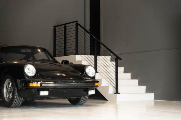 White stair in a gray showroom garage with black horizontal rod railing behind a classic black sports car.
