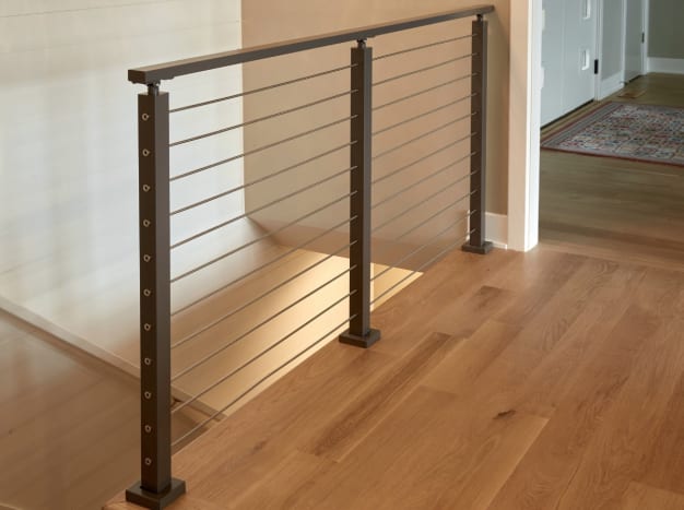 Bronze-finish cable posts and top rail guard a stair opening on a white oak floor.