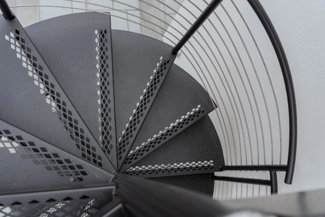 Overhead view of perforated black steel spiral treads with curved cable railing.
