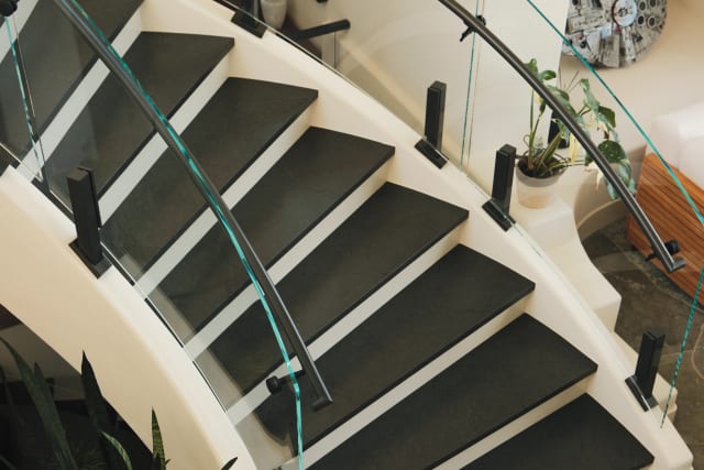Overhead view of curved glass railing on black talons and a dark handrail along a white curved stair.