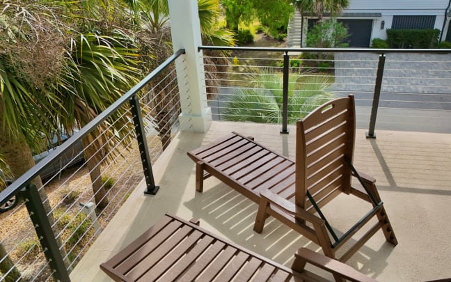 Black cable railing surrounds a balcony with wooden loungers overlooking palms.