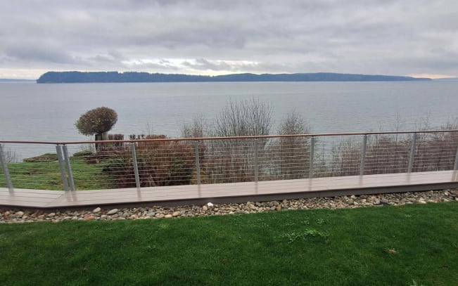 Polished stainless posts with cable infill line a curving IPE walkway along a lawn overlooking the water.
