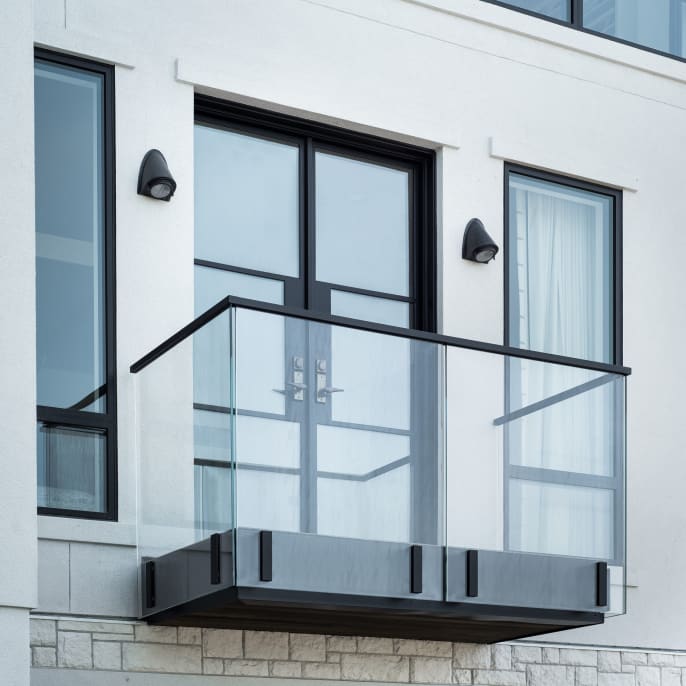 Frameless glass Juliet balcony with black side-mount talons and a black cap rail beneath French doors.