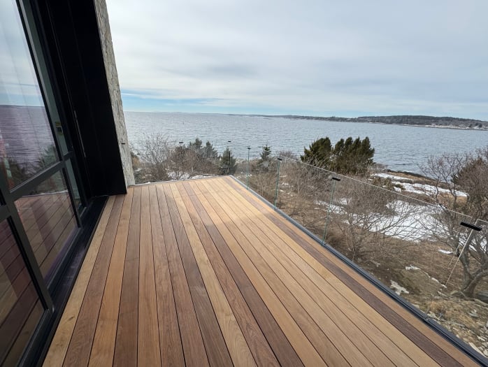 Frameless laminated glass in a recessed base rail lines an Ipe balcony looking out to a rocky coastline.