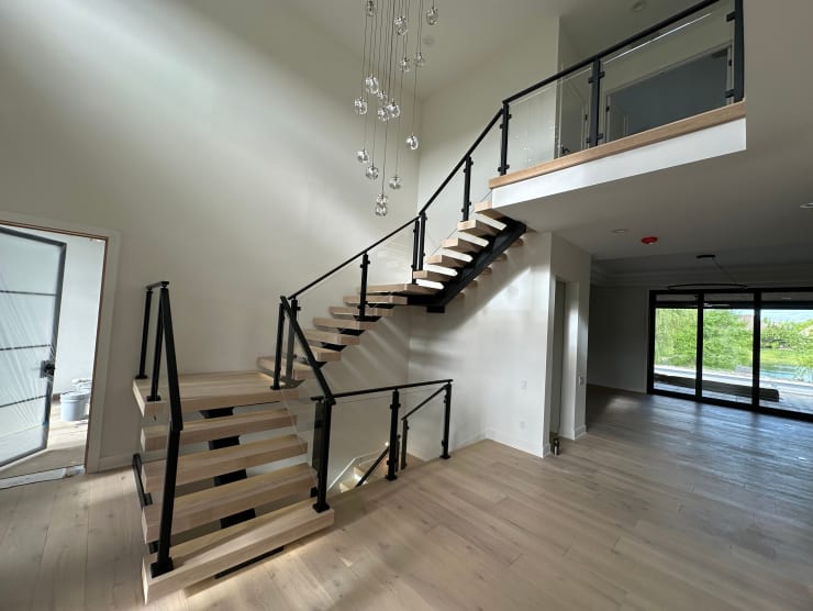 Black mono stringer switchback stair with white oak treads and black post-to-post glass railing continuing to an open loft in a bright foyer.