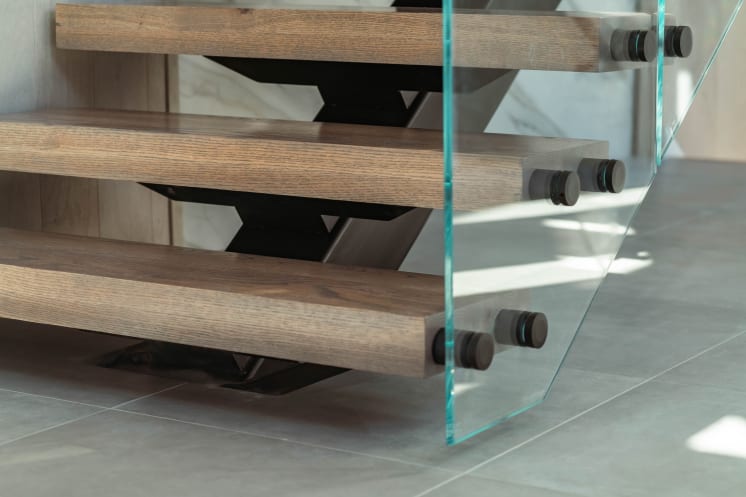 Close view of black standoff pins holding glass to oak treads on a black mono stringer.