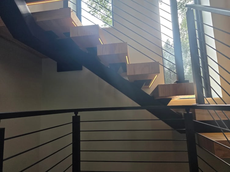 Floating stair with LED-lit treads above a black cable railing at the landing