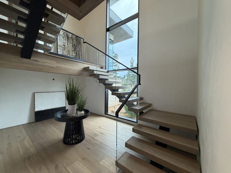 White oak FLIGHT Mono switchback with frameless glass and black handrail by a tall window
