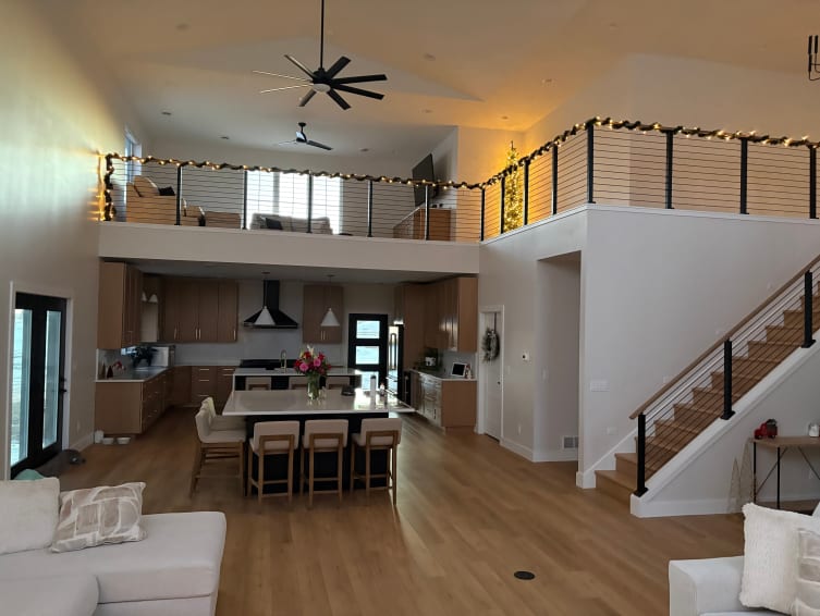 Black cable railing with a wood cap follows a stair and wraps a loft above an open kitchen and living room.