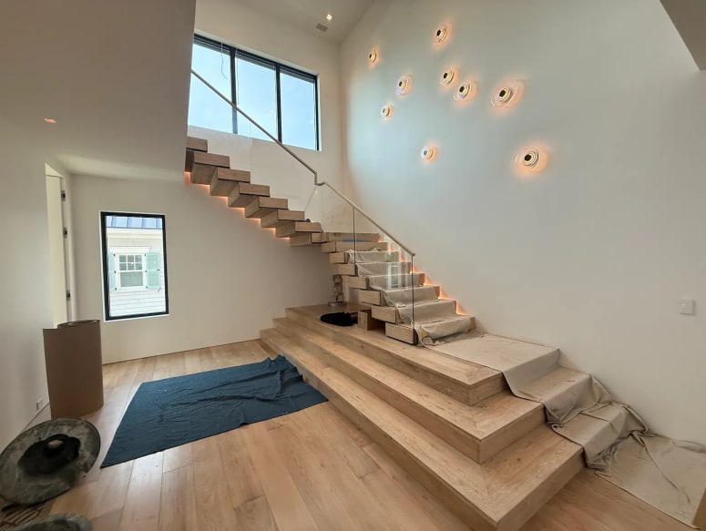 Connected white oak Stack treads with LED lighting and frameless glass beneath a wall of round sconces