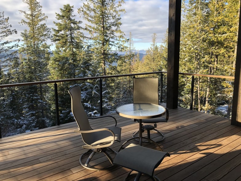 Black cable railing with wood cap around a covered deck looking out to snowy evergreens.