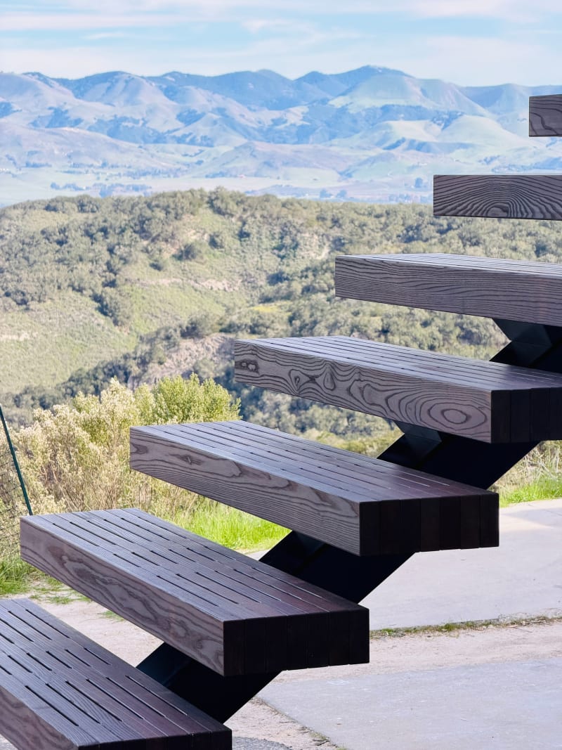 Mocha-stained exterior Endurance treads on a black stringer frame a sweeping view of green hills and mountains.