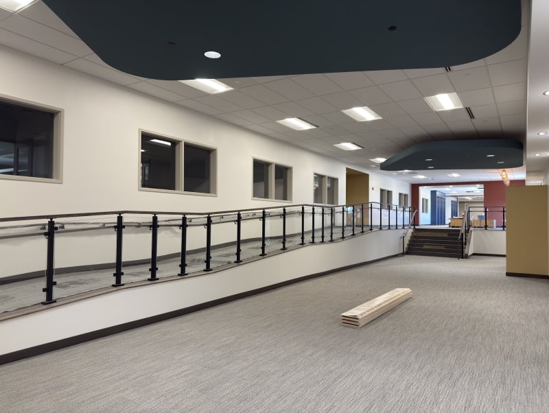 Long accessible ramp lined with black-post glass railing and handrails in a commercial corridor