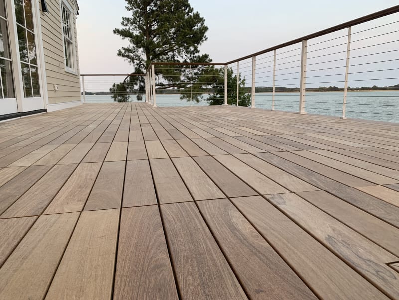 A wide hardwood deck overlooking a lake, edged by white-post cable railing with a wood cap rail.