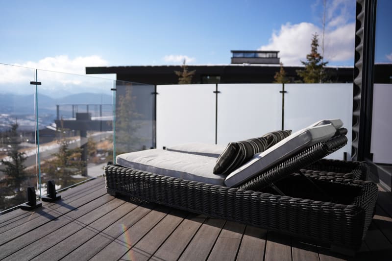 Clear and frosted glass panels on talons surround a deck with wicker loungers and mountain views.