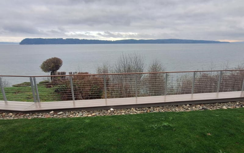 Polished stainless posts with cable infill line a curving IPE walkway along a lawn overlooking the water.