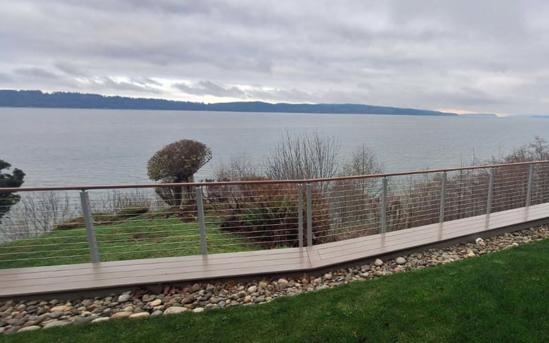 Stainless cable railing follows an angled IPE deck path above a rock border with island views.